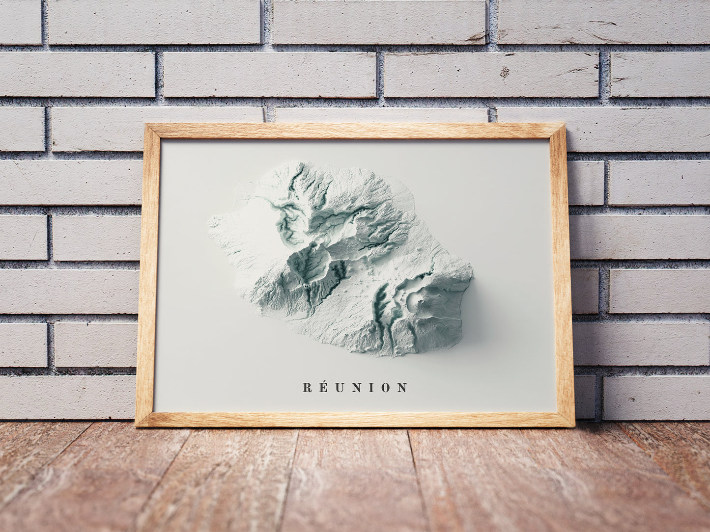 Reunion, France, shaded relief map in a wooden frame. Realistic terrain art print for home decor, displayed against a brick wall