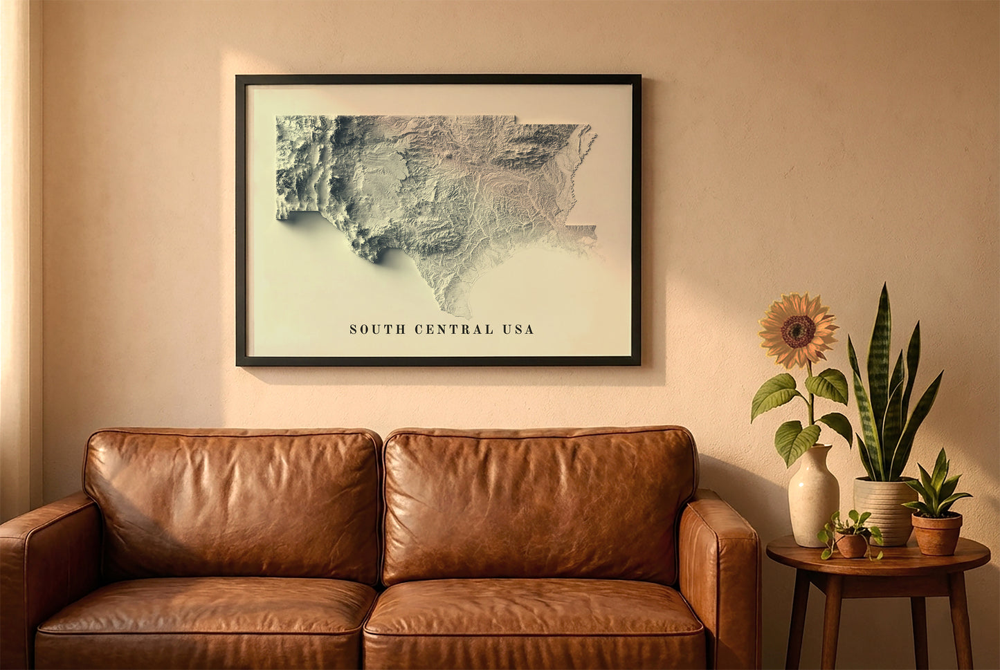South Central USA relief map in a black frame above a brown leather sofa. Boho living room with warm sunlight, sunflower, and indoor plants on a wooden side table