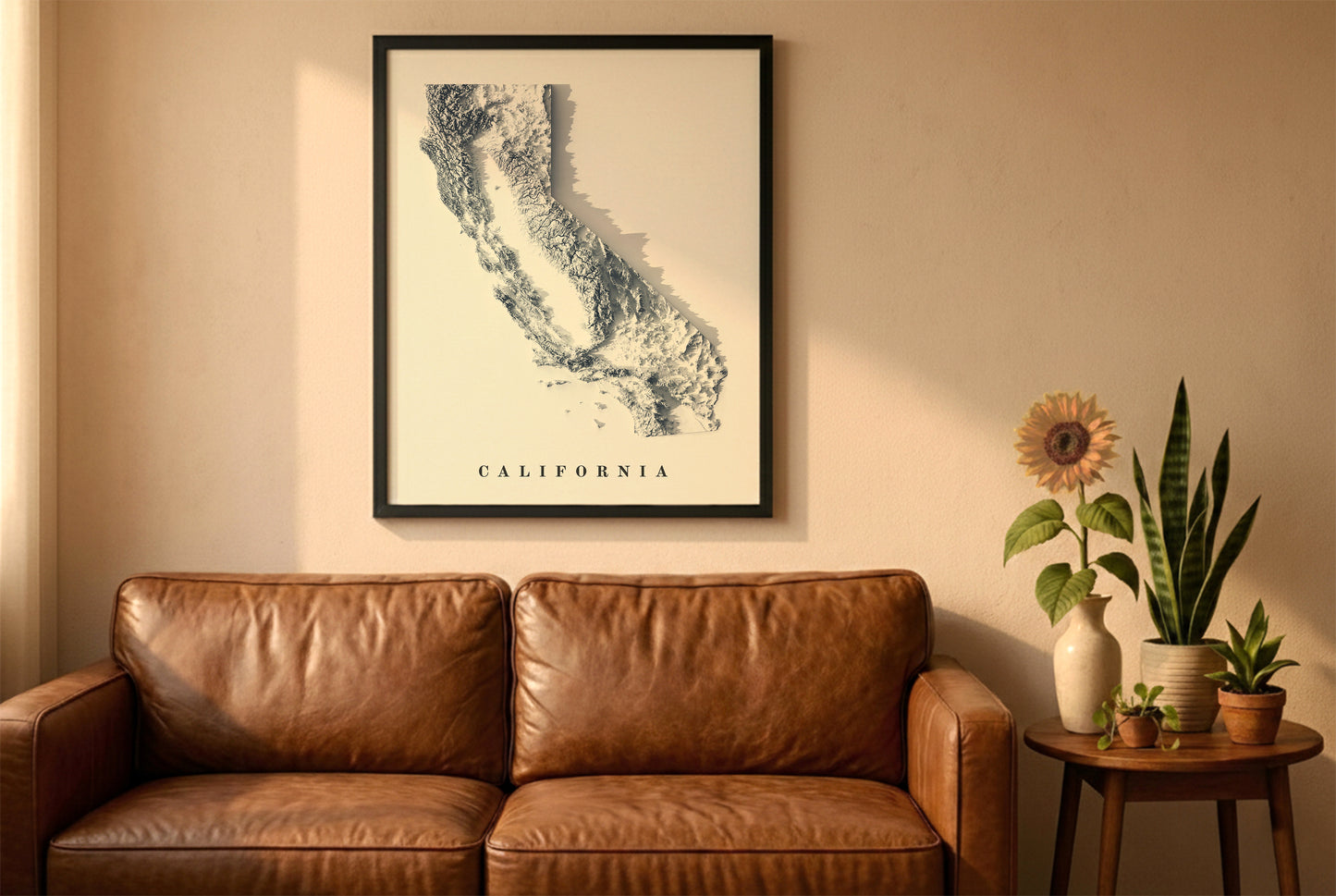 California relief map in a black frame above a brown leather sofa. Boho living room with warm sunlight, sunflower, and indoor plants on a wooden side table