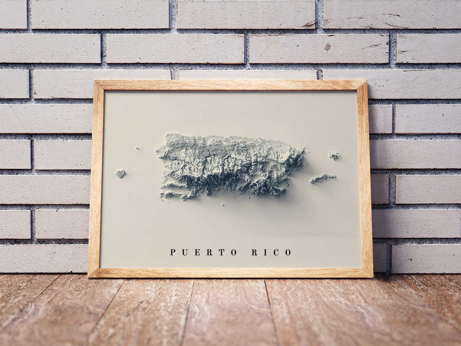 Puerto Rico shaded relief map in a wooden frame. Realistic terrain art print for home decor, displayed against a brick wall