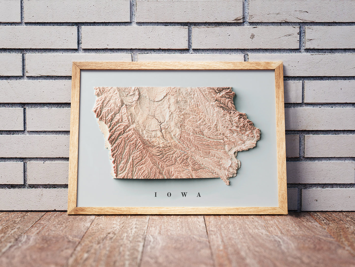 Iowa shaded relief map in a wooden frame. Realistic terrain art print for home decor, displayed against a brick wall