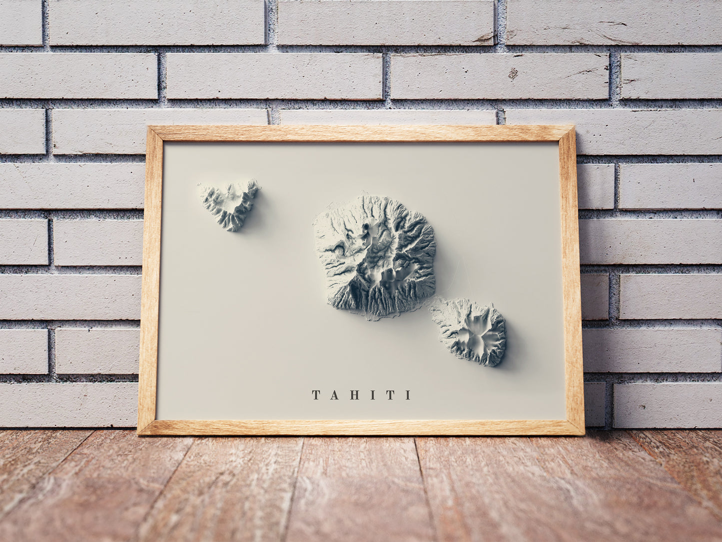 Tahiti shaded relief map in a wooden frame. Realistic terrain art print for home decor, displayed against a brick wall