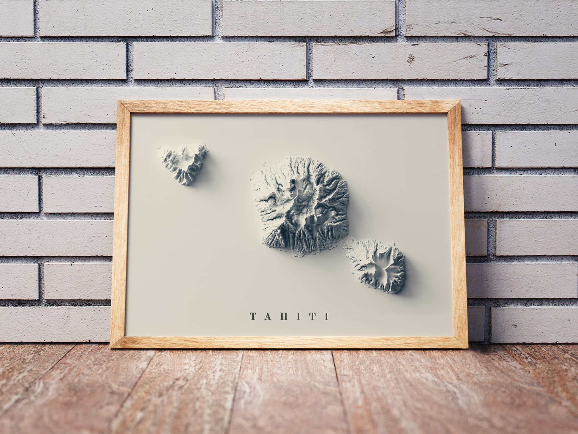 Tahiti shaded relief map in a wooden frame. Realistic terrain art print for home decor, displayed against a brick wall