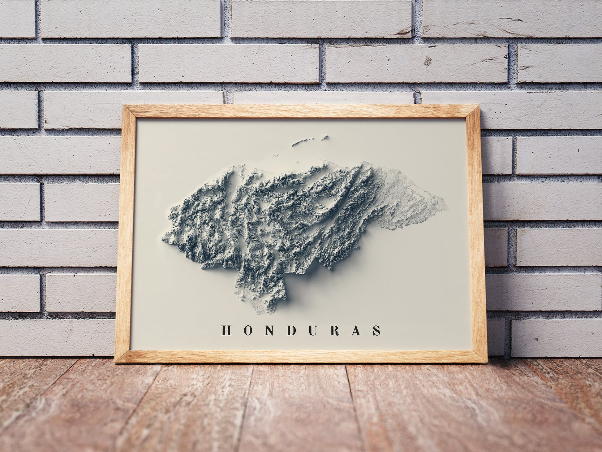 Honduras shaded relief map in a wooden frame. Realistic terrain art print for home decor, displayed against a brick wall