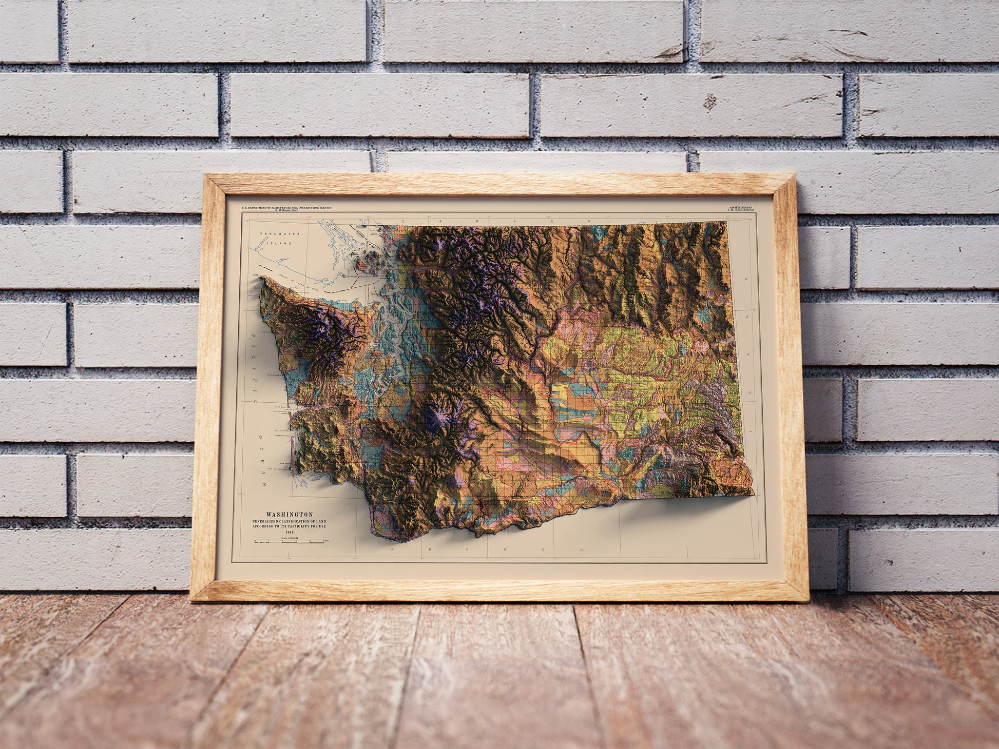 Vintage Washington shaded relief map in a wooden frame. Realistic terrain art print for home decor, displayed against a brick wall
