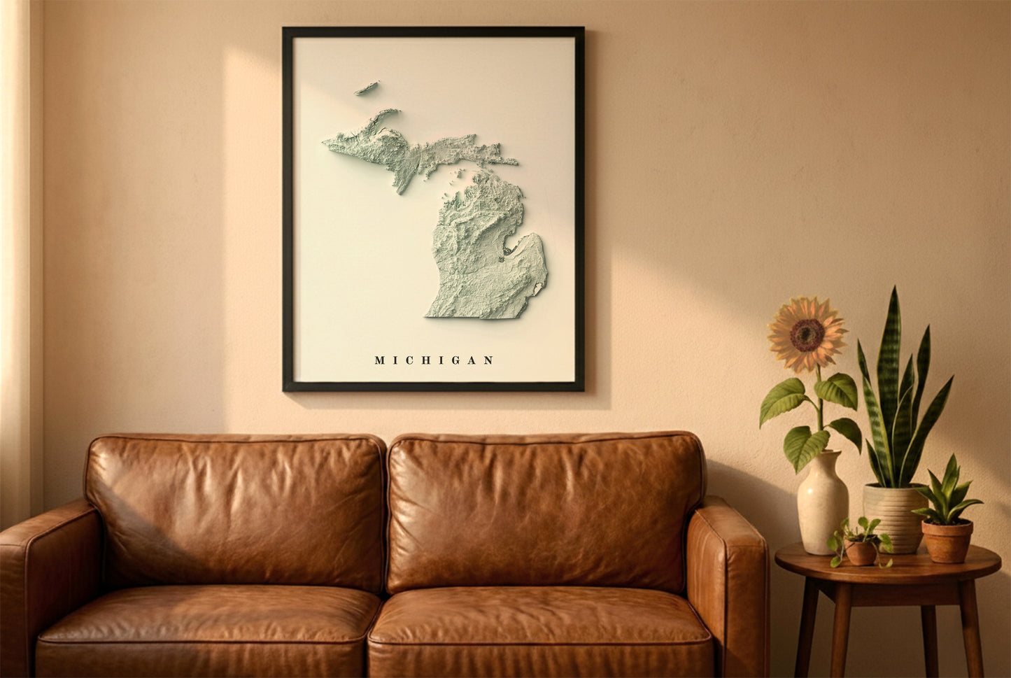 Michigan relief map in a black frame above a brown leather sofa. Boho living room with warm sunlight, sunflower, and indoor plants on a wooden side table