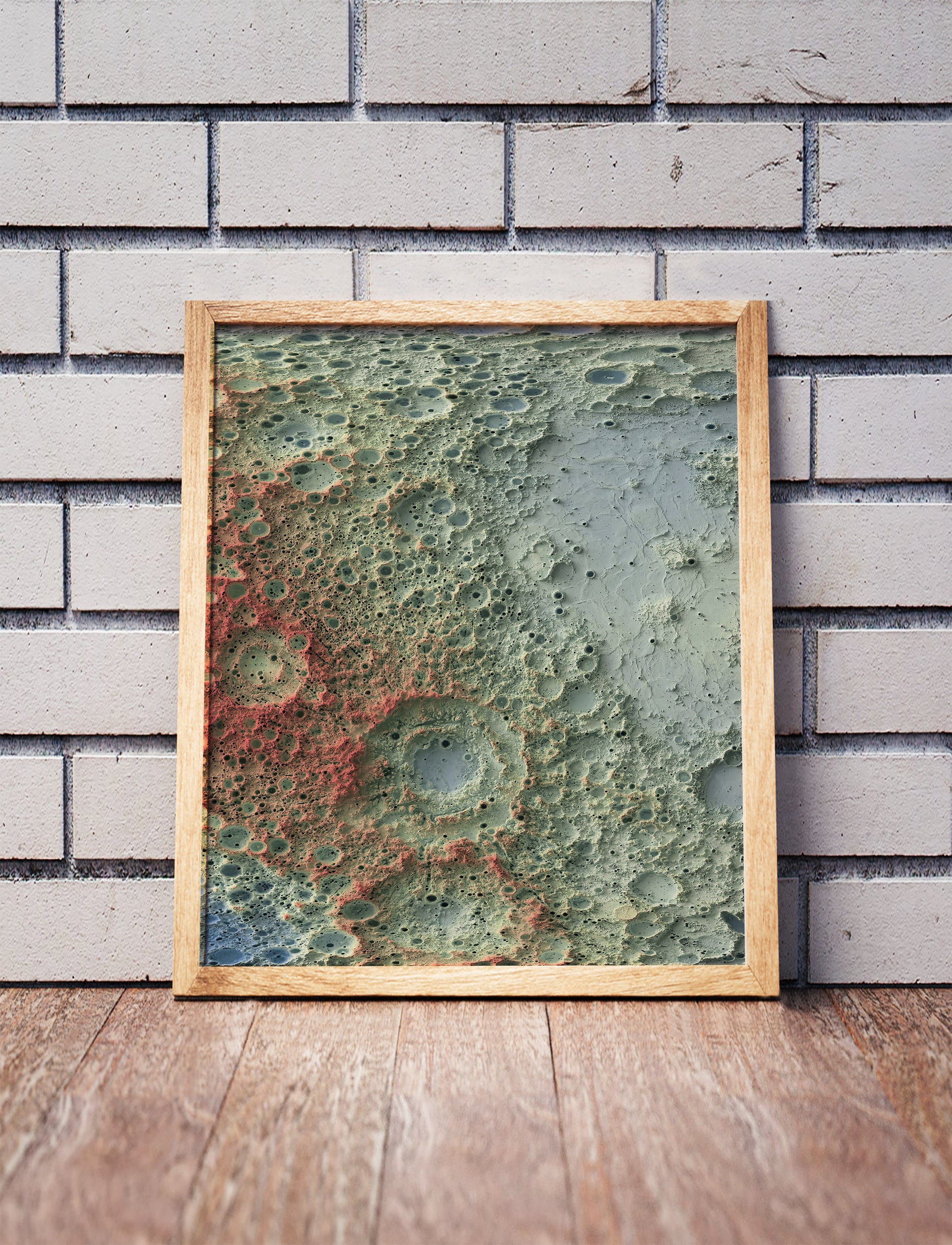 Moon shaded relief map in a wooden frame. Realistic terrain art print for home decor, displayed against a brick wall