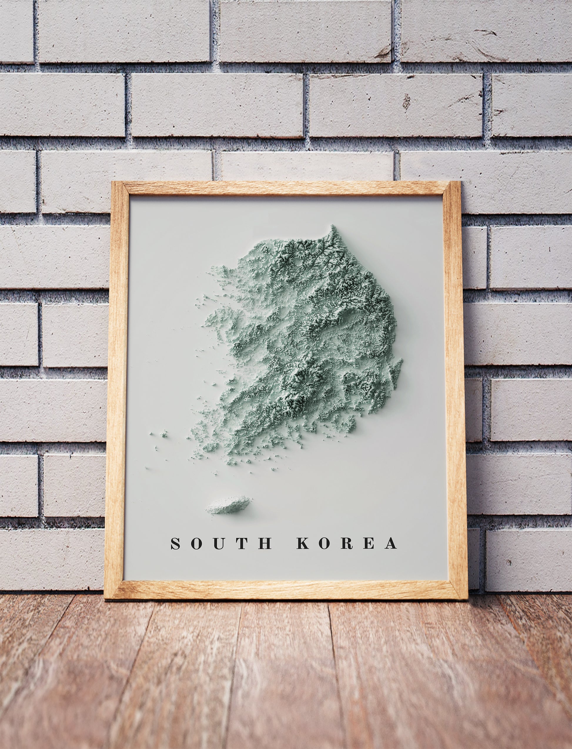 South Korea shaded relief map in a wooden frame. Realistic terrain art print for home decor, displayed against a brick wall