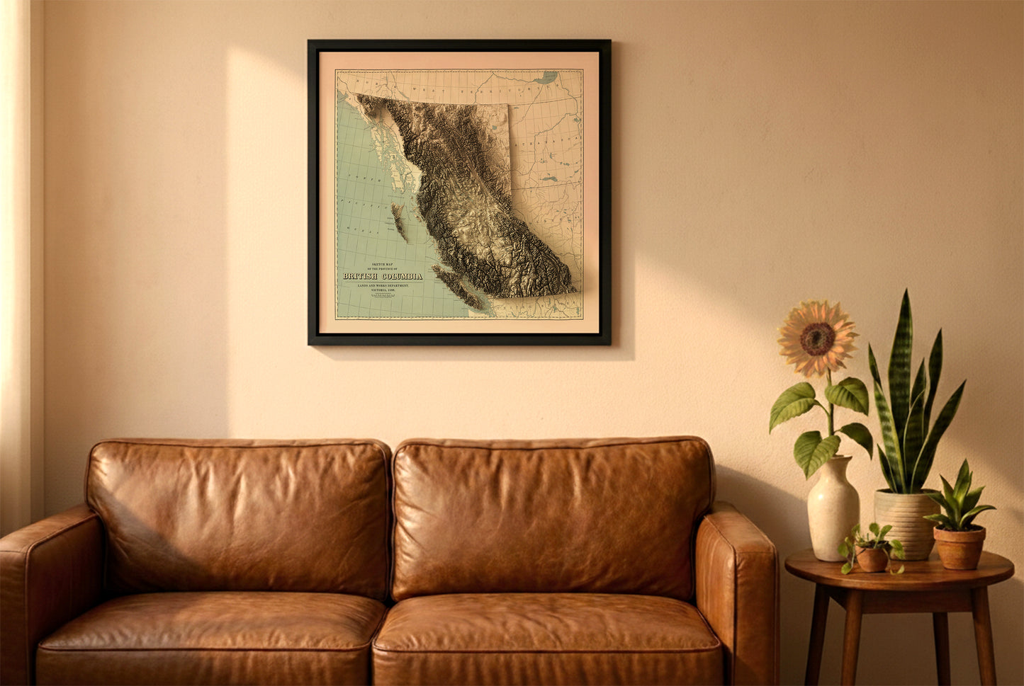British Columbia, Canada, vintage relief map in a black frame above a brown leather sofa. Boho living room with warm sunlight, sunflower, and indoor plants on a wooden side table