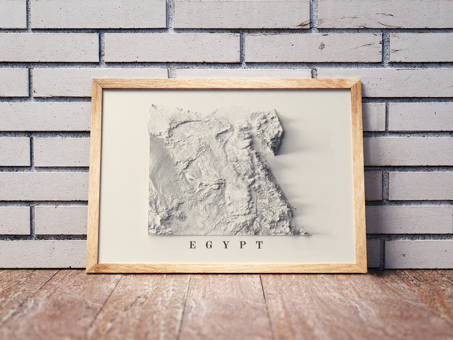 Egypt shaded relief map in a wooden frame. Realistic terrain art print for home decor, displayed against a brick wall