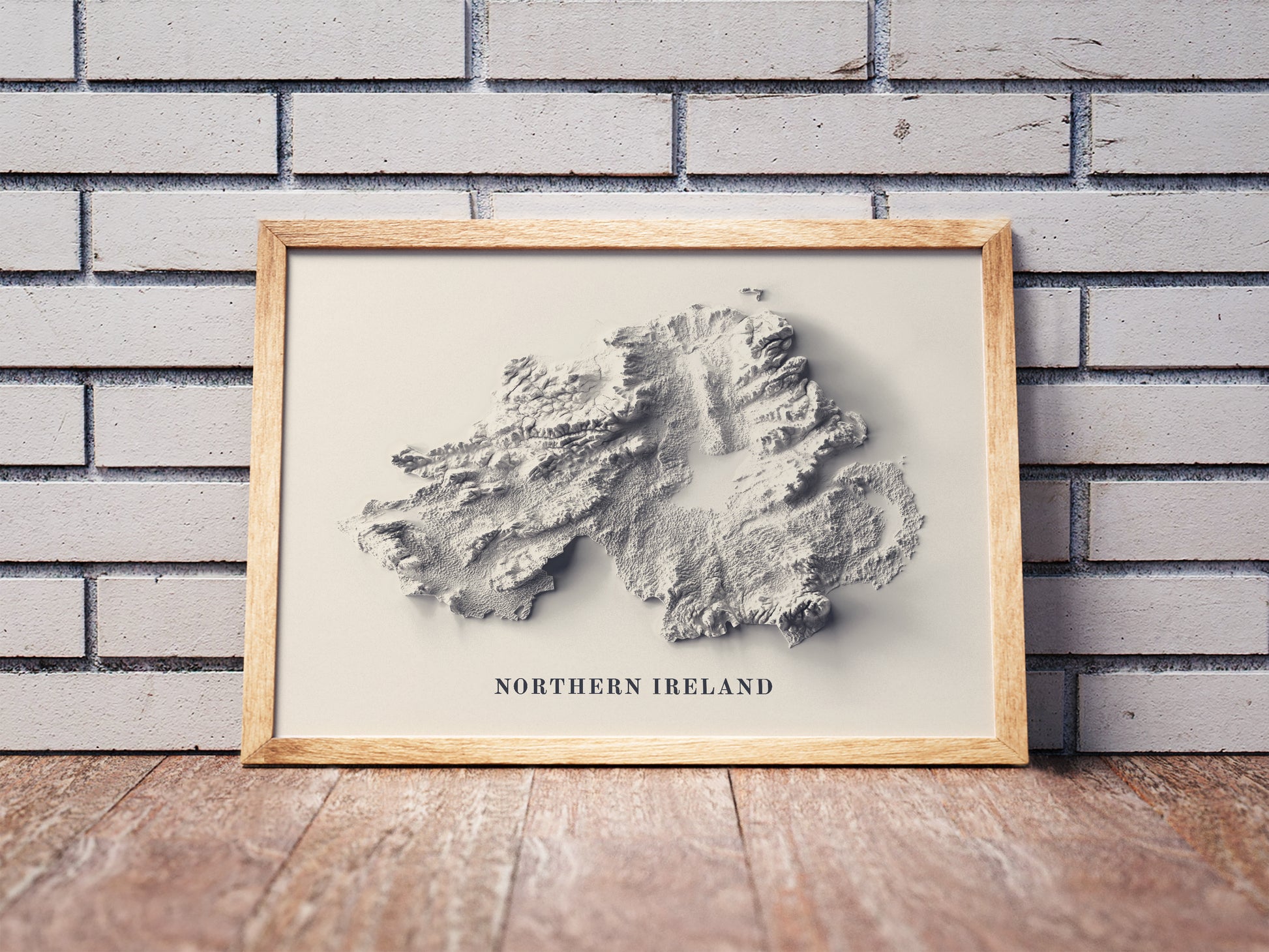 northern ireland shaded relief map in a wooden frame. Realistic terrain art print for home decor, displayed against a brick wall