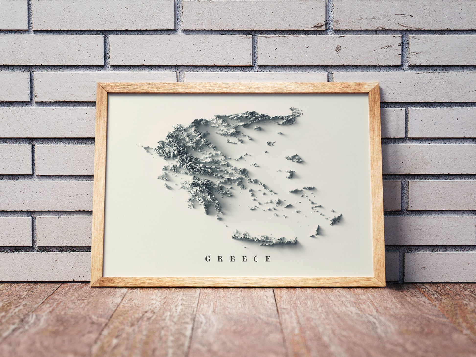 Greece shaded relief map in a wooden frame. Realistic terrain art print for home decor, displayed against a brick wall