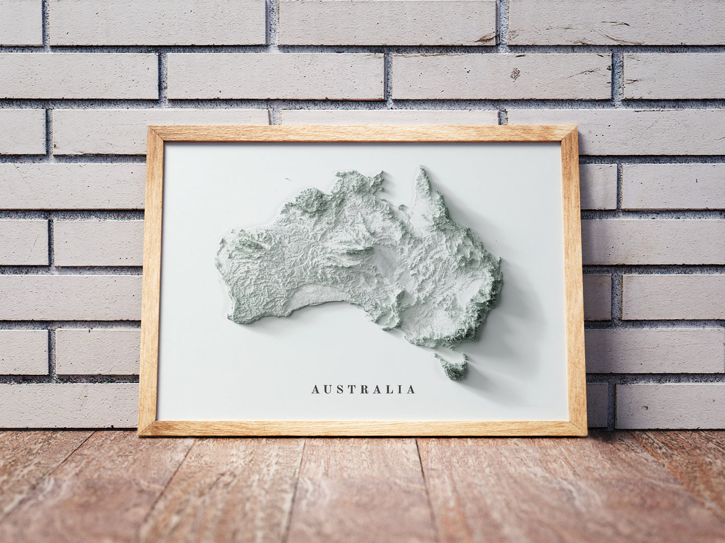 Australia shaded relief map in a wooden frame. Realistic terrain art print for home decor, displayed against a brick wall