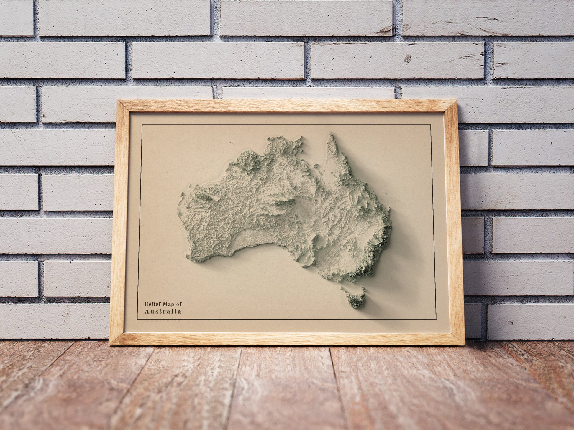 Australia shaded relief map in a wooden frame. Realistic terrain art print for home decor, displayed against a brick wall