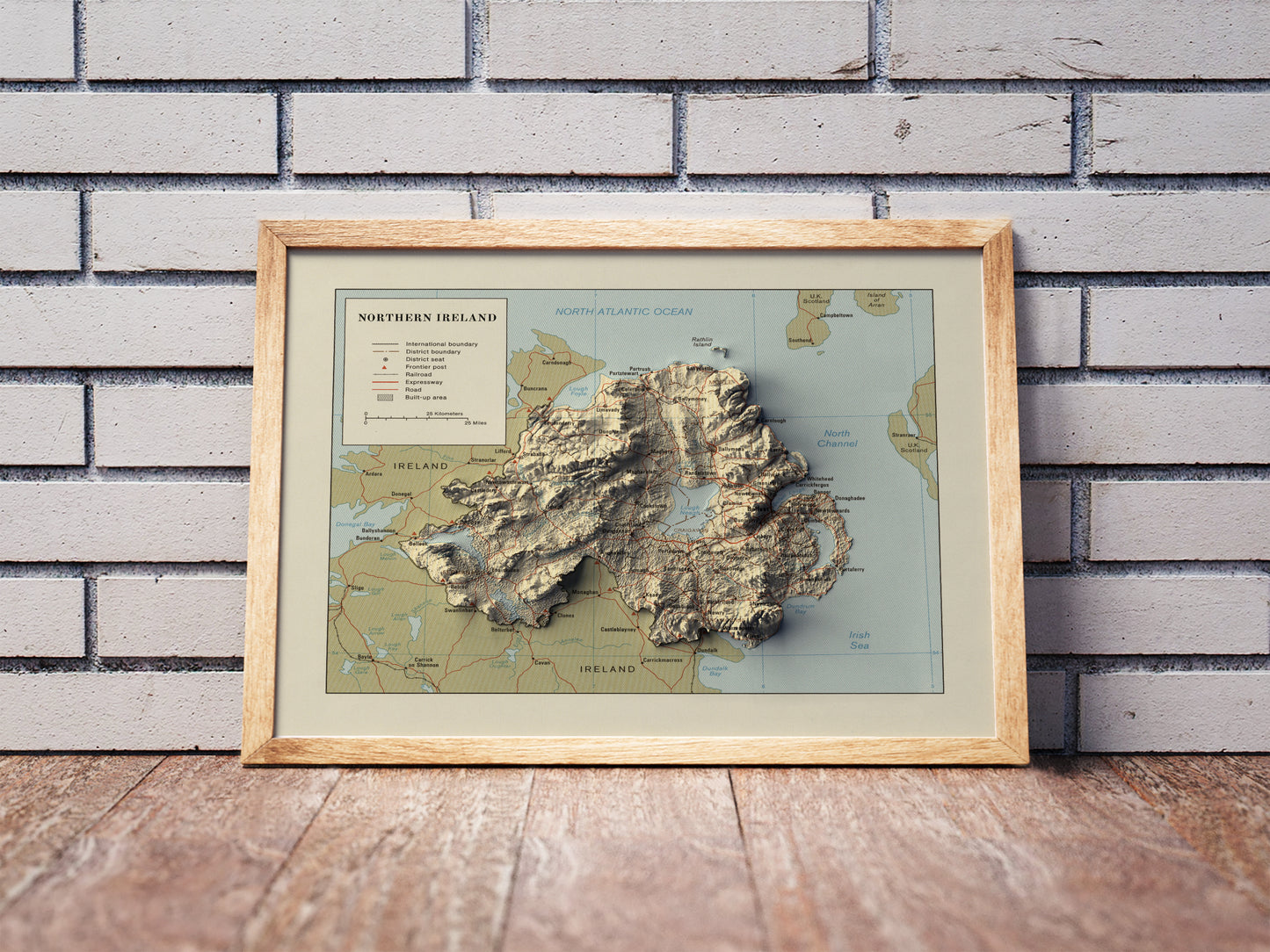 northern ireland vintage shaded relief map in a wooden frame. Realistic terrain art print for home decor, displayed against a brick wall