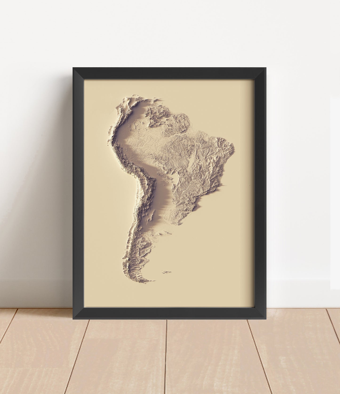 South America shaded relief map in a wooden frame. Realistic terrain art print for home decor, displayed against a brick wall