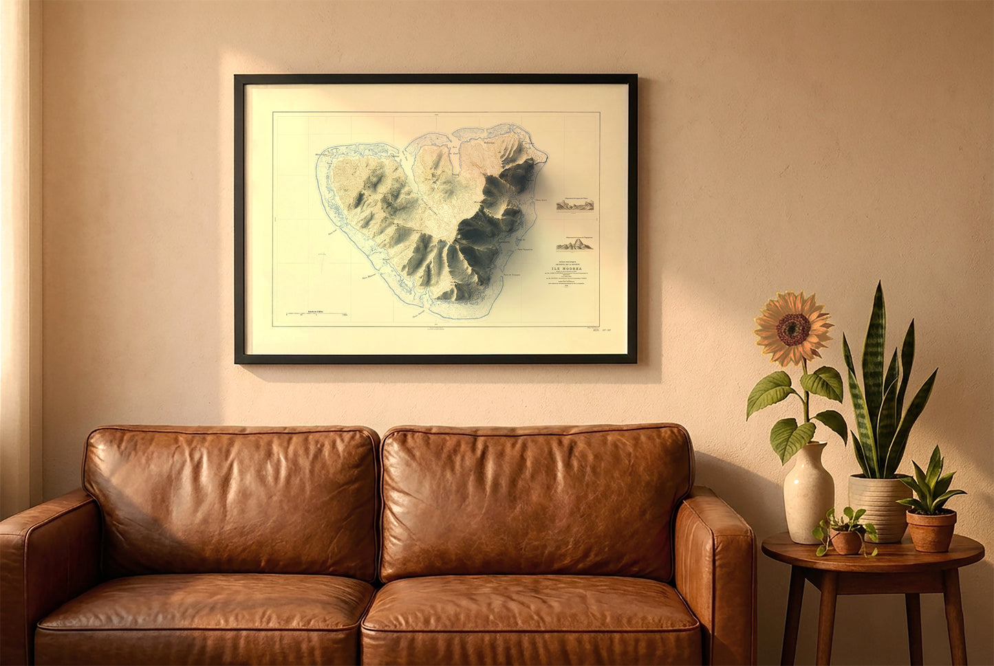 Moorea vintage relief map in a black frame above a brown leather sofa. Boho living room with warm sunlight, sunflower, and indoor plants on a wooden side table