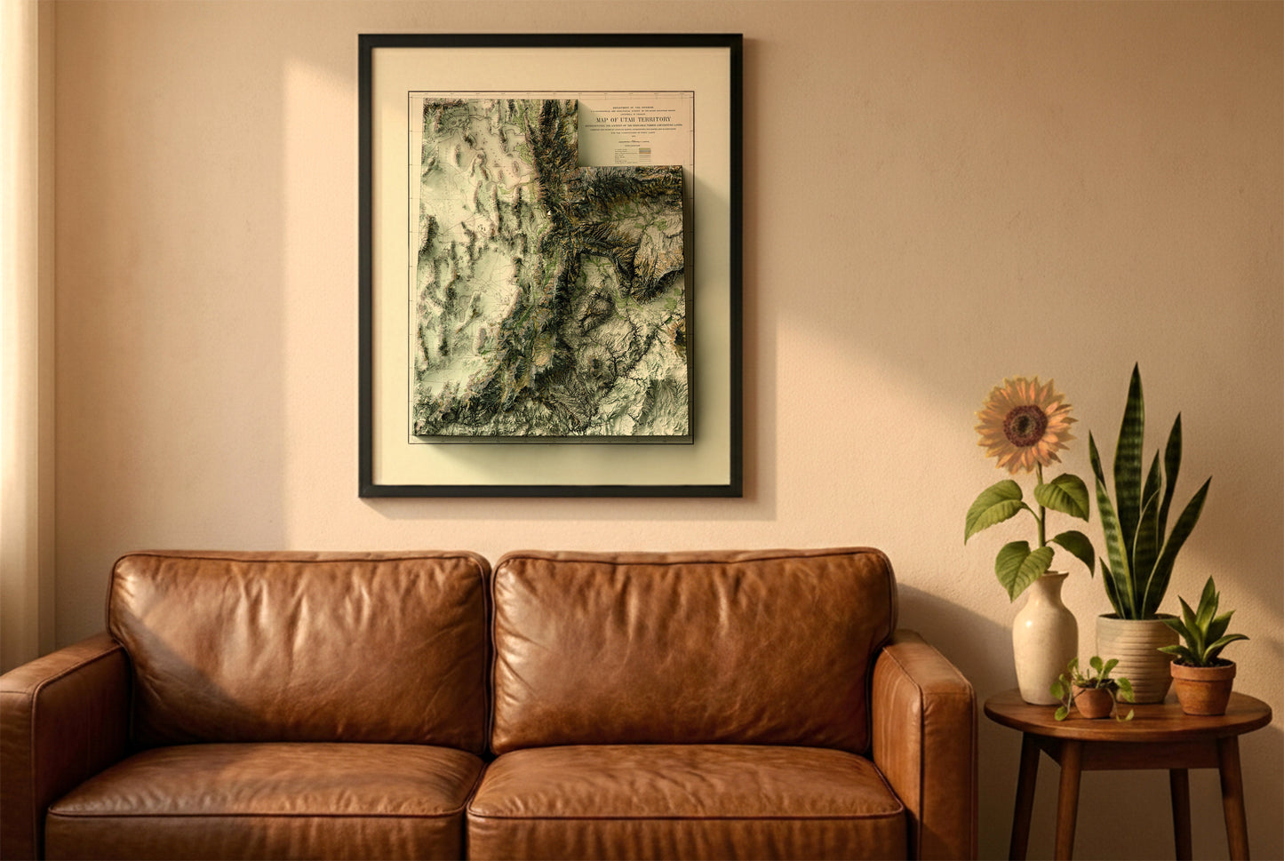 Utah vintage relief map in a black frame above a brown leather sofa. Boho living room with warm sunlight, sunflower, and indoor plants on a wooden side table