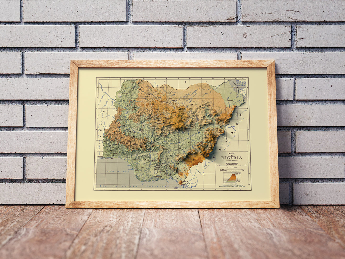 Vintage Nigeria shaded relief map in a wooden frame. Realistic terrain art print for home decor, displayed against a brick wall