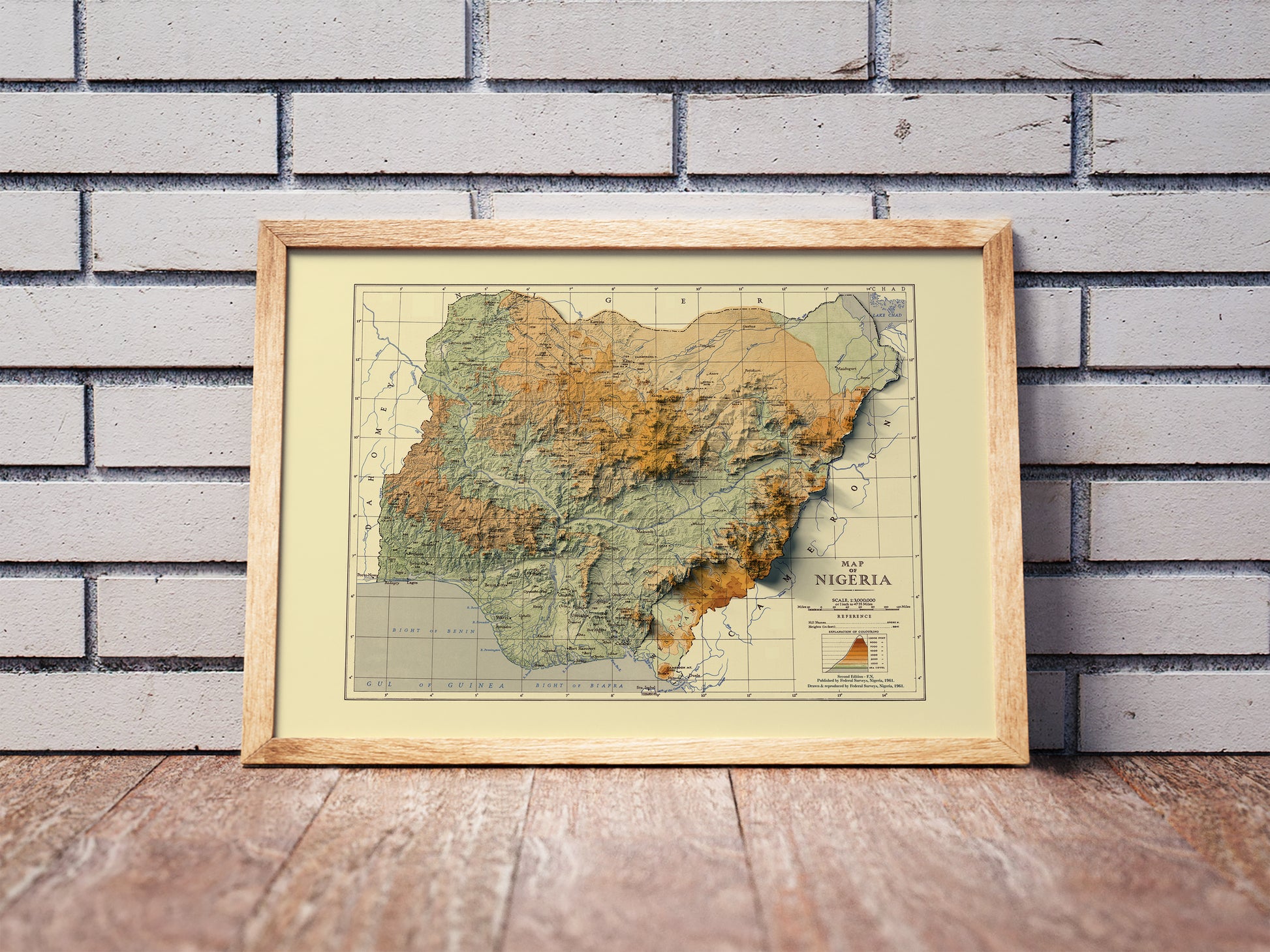Vintage Nigeria shaded relief map in a wooden frame. Realistic terrain art print for home decor, displayed against a brick wall