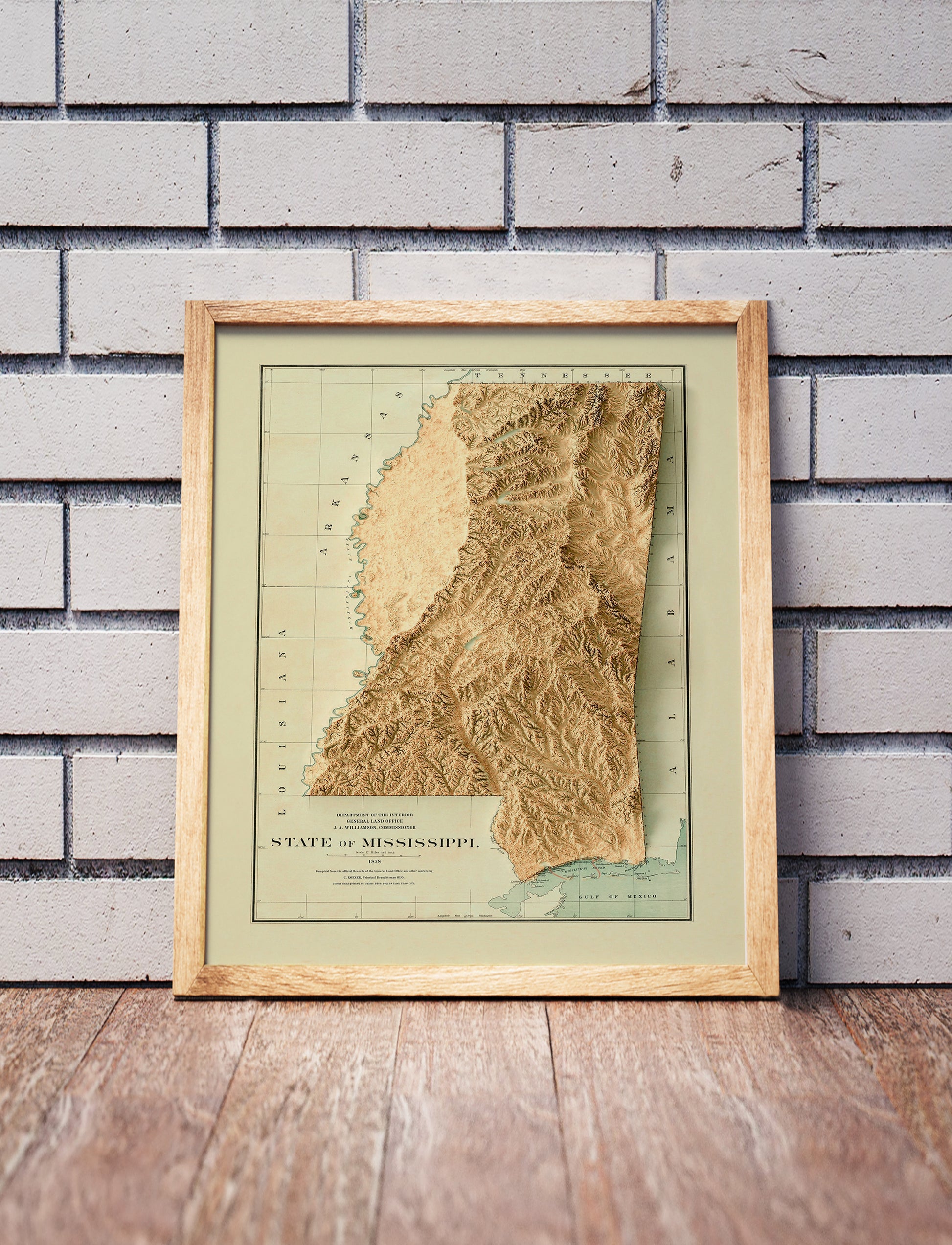 Vintage Mississippi shaded relief map in a wooden frame. Realistic terrain art print for home decor, displayed against a brick wall