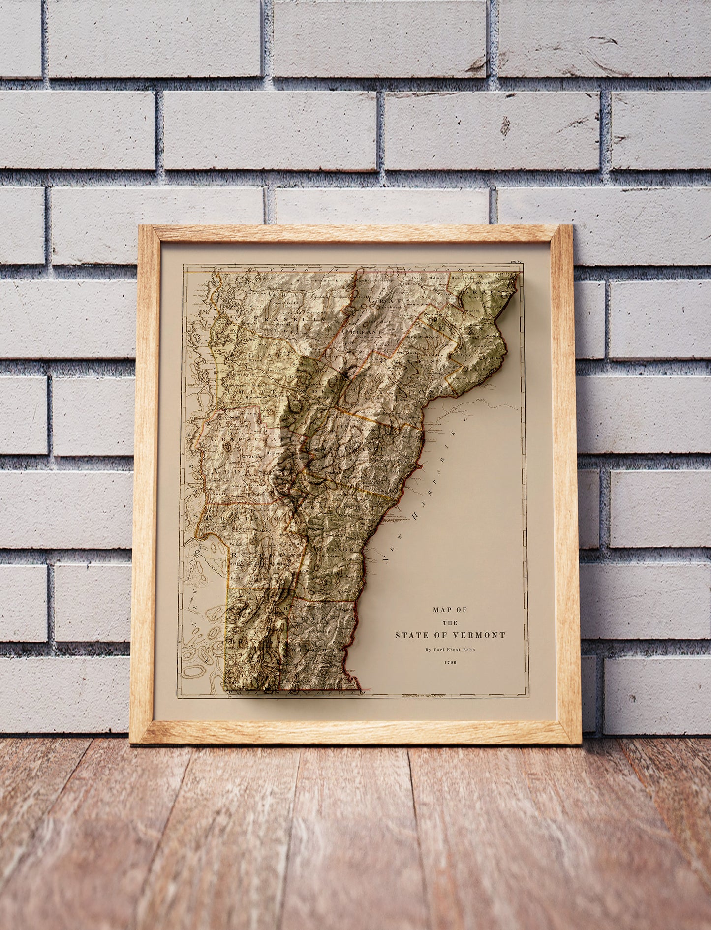 Vintage Vermont shaded relief map in a wooden frame. Realistic terrain art print for home decor, displayed against a brick wall