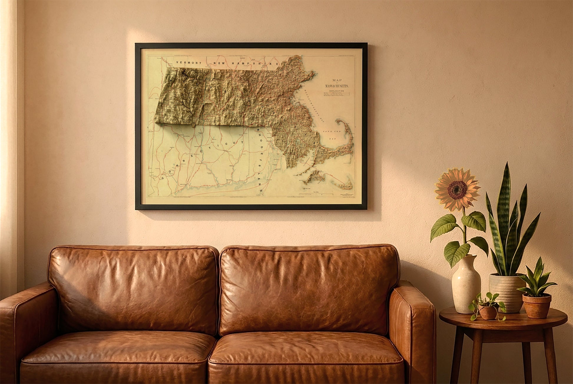 Massachusetts vintage relief map in a black frame above a brown leather sofa. Boho living room with warm sunlight, sunflower, and indoor plants on a wooden side table