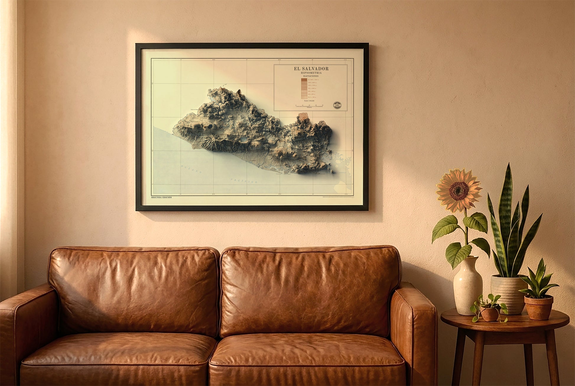 El Salvador vintage relief map in a black frame above a brown leather sofa. Boho living room with warm sunlight, sunflower, and indoor plants on a wooden side table