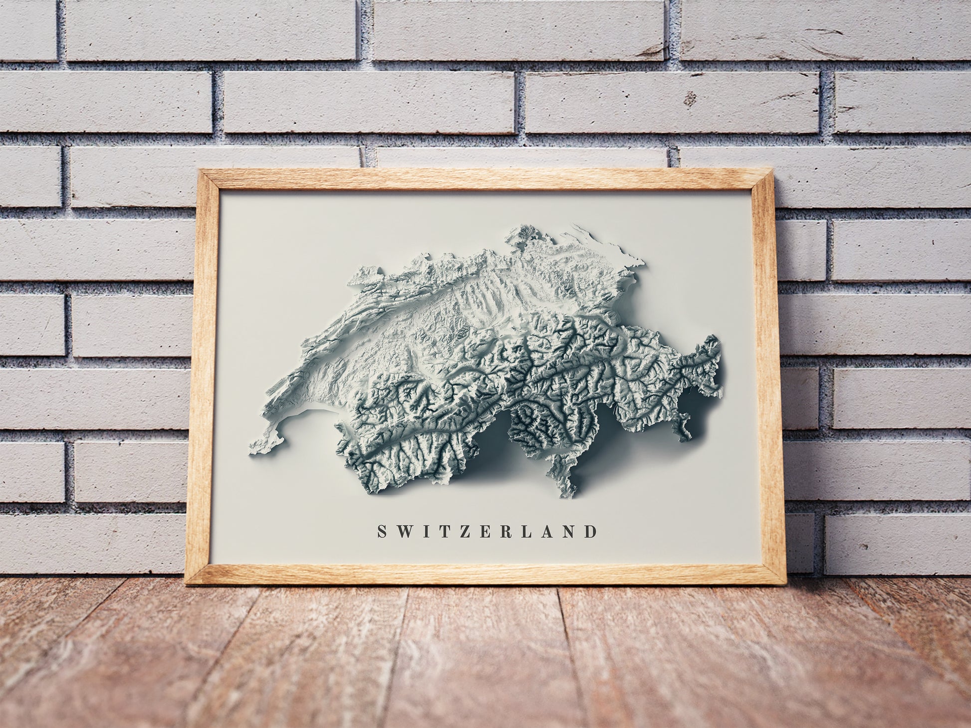 Switzerland shaded relief map in a wooden frame. Realistic terrain art print for home decor, displayed against a brick wall