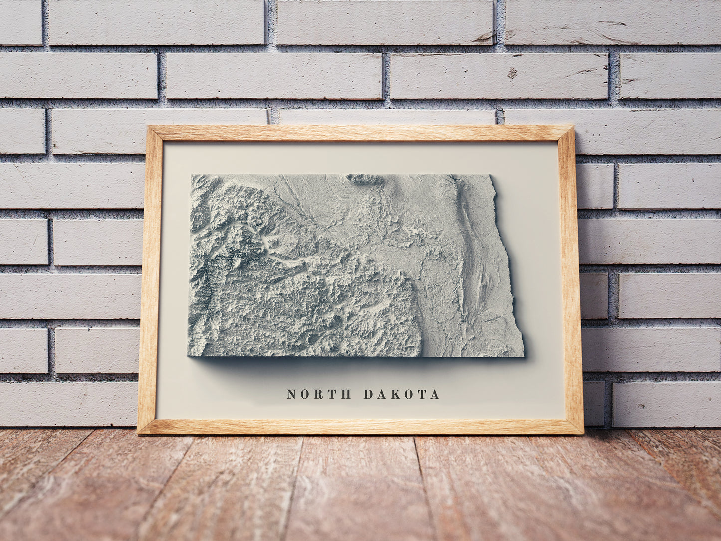 North Dakota shaded relief map in a wooden frame. Realistic terrain art print for home decor, displayed against a brick wall