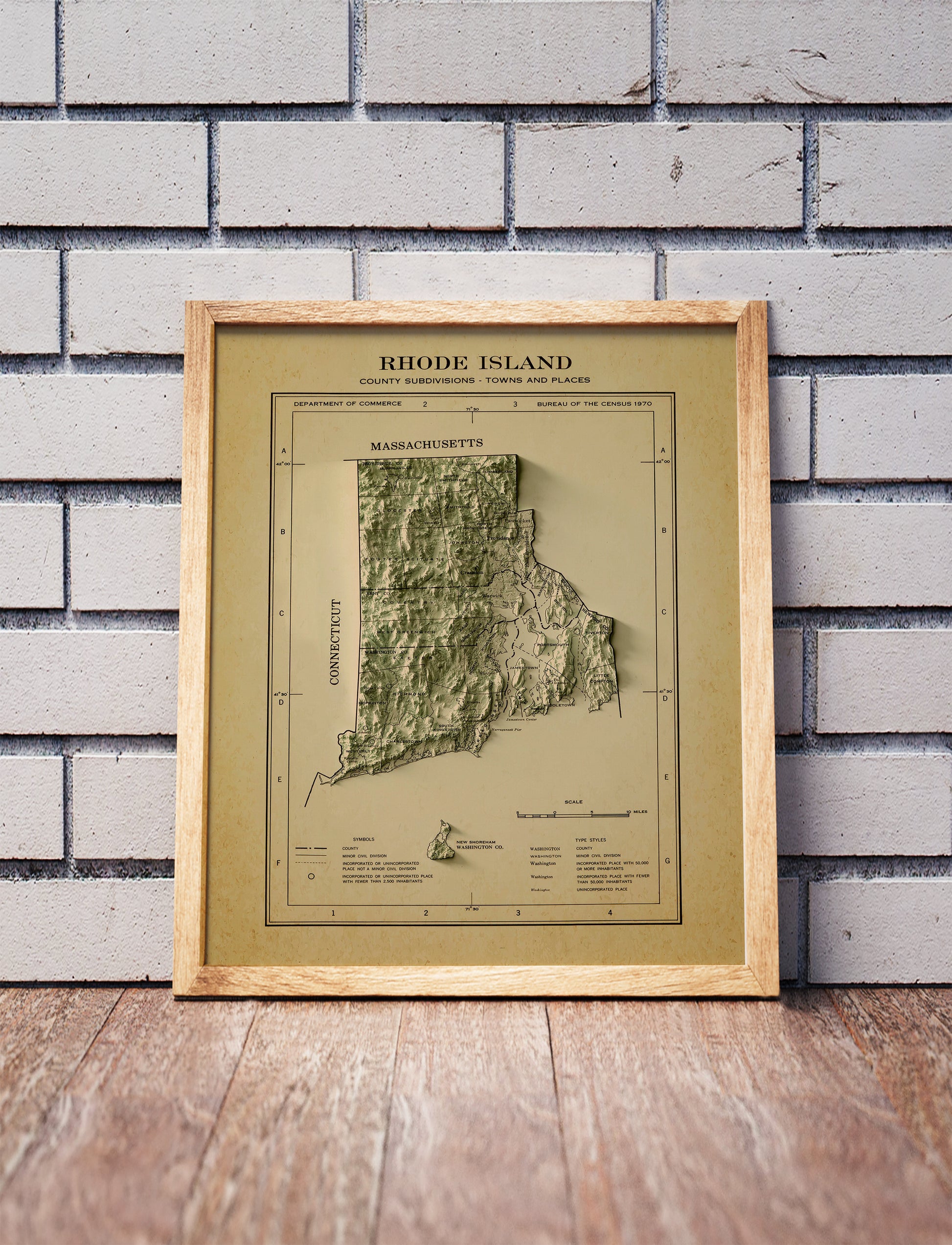 Vintage Rhode Island shaded relief map in a wooden frame. Realistic terrain art print for home decor, displayed against a brick wall