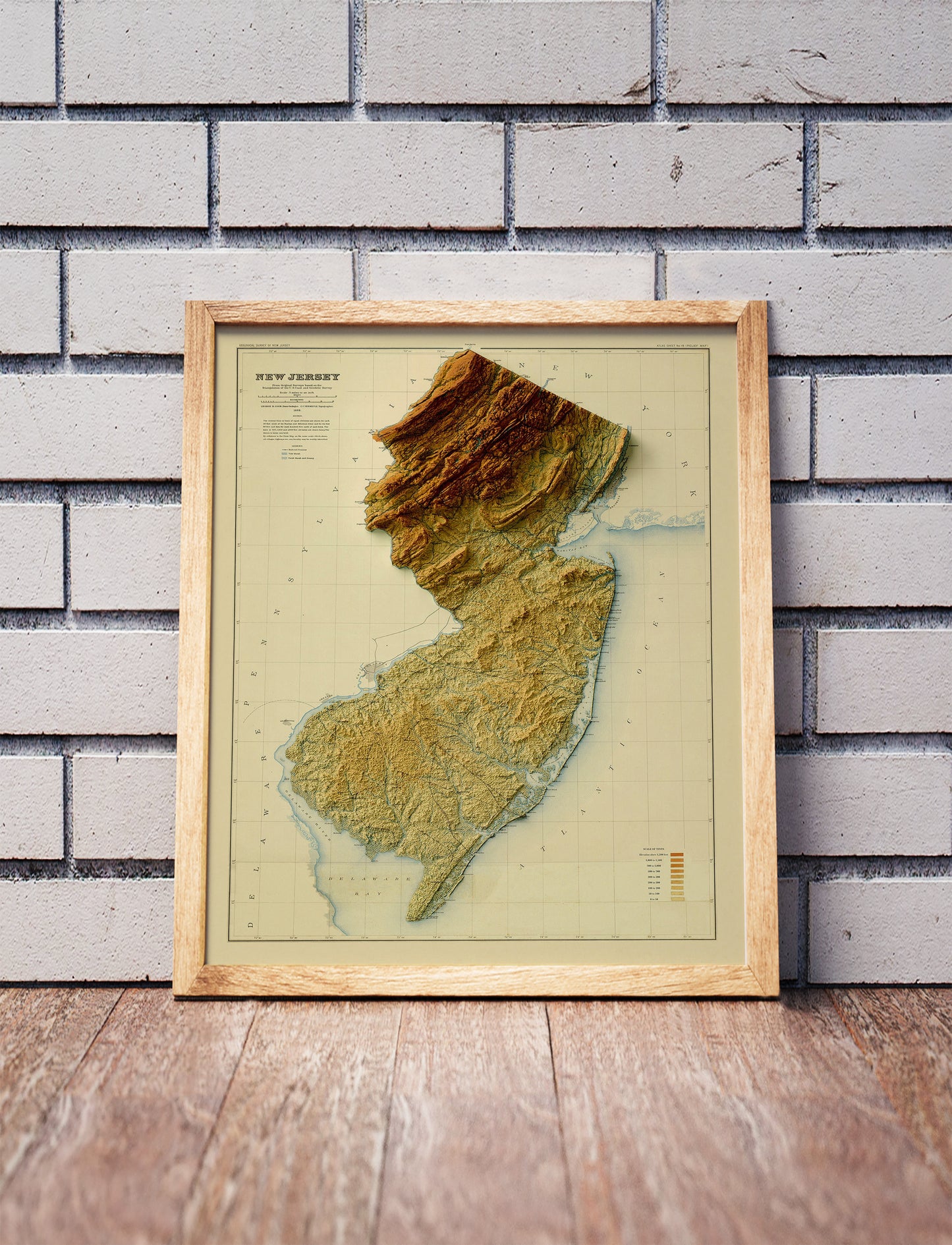Vintage New Jersey shaded relief map in a wooden frame. Realistic terrain art print for home decor, displayed against a brick wall