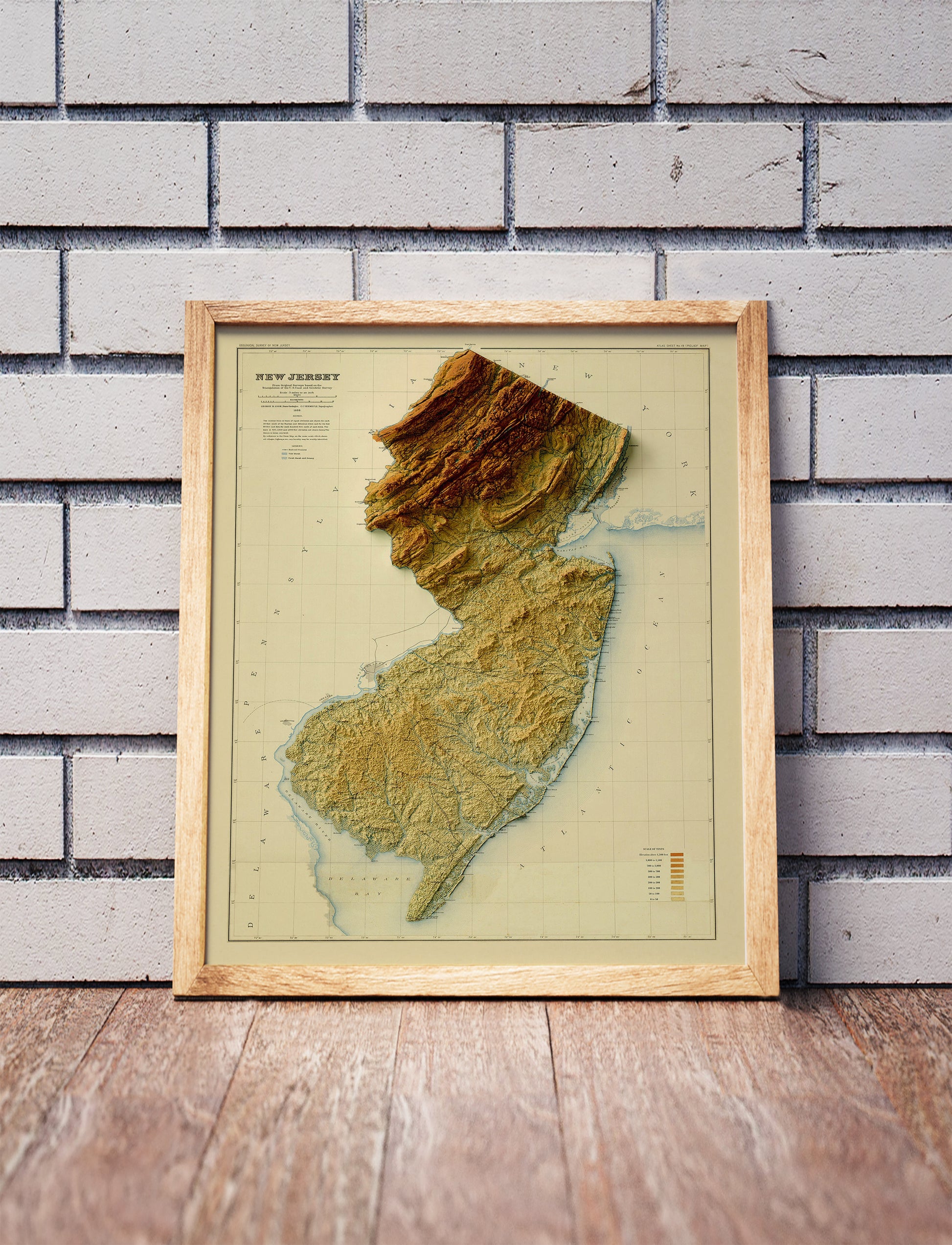 Vintage New Jersey shaded relief map in a wooden frame. Realistic terrain art print for home decor, displayed against a brick wall