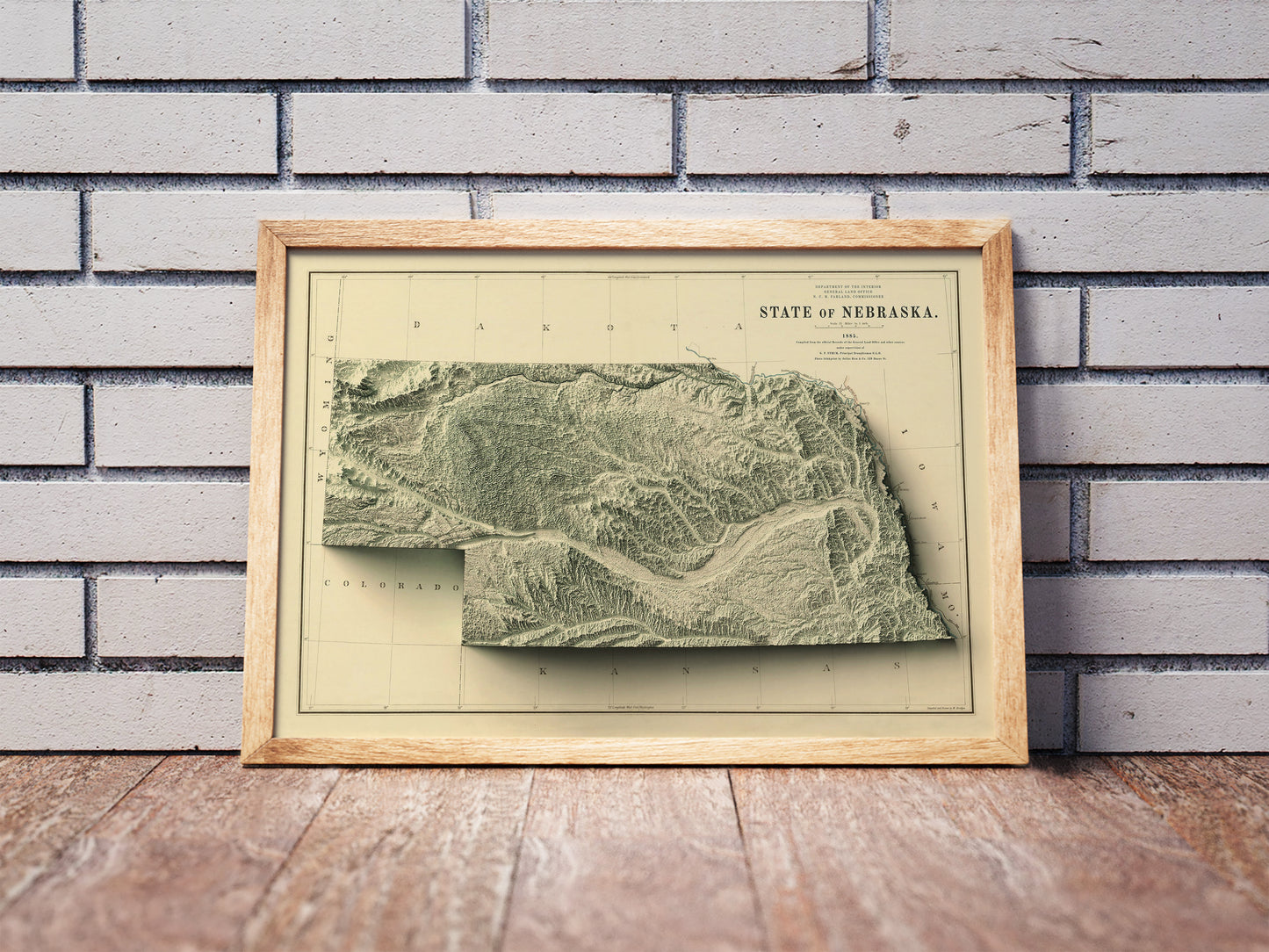 Vintage Nebraska shaded relief map in a wooden frame. Realistic terrain art print for home decor, displayed against a brick wall