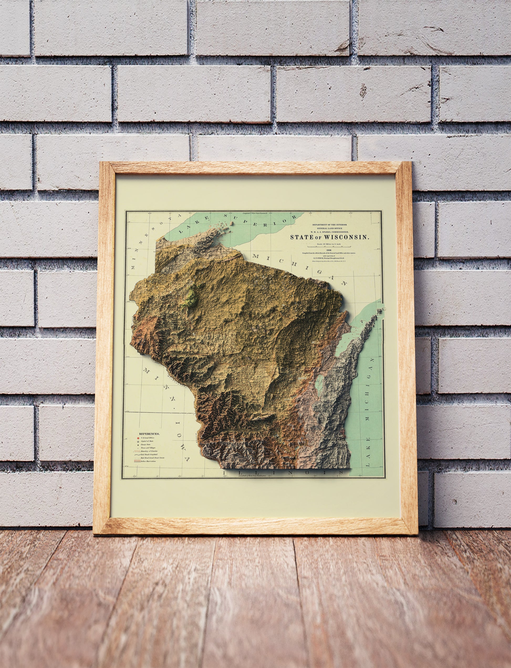 Vintage Wisconsin shaded relief map in a wooden frame. Realistic terrain art print for home decor, displayed against a brick wall