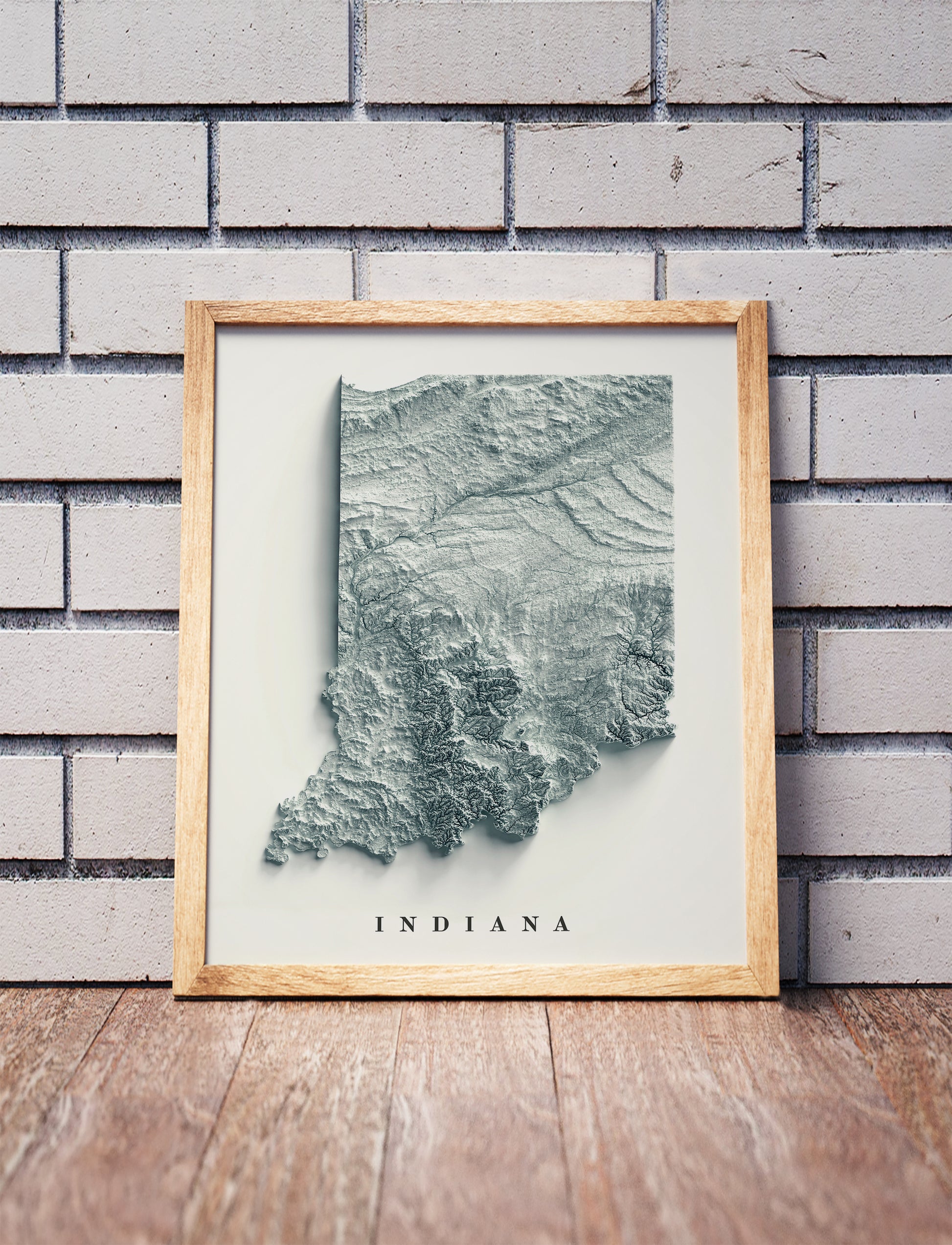 Indiana shaded relief map in a wooden frame. Realistic terrain art print for home decor, displayed against a brick wall