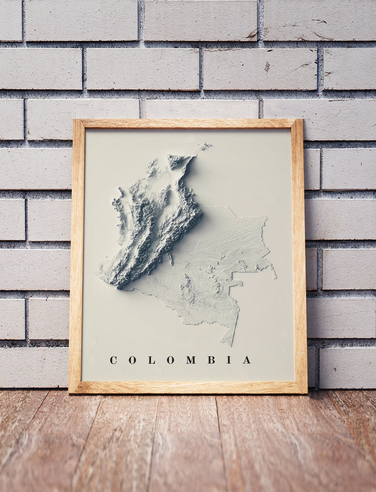 Colombia shaded relief map in a wooden frame. Realistic terrain art print for home decor, displayed against a brick wall