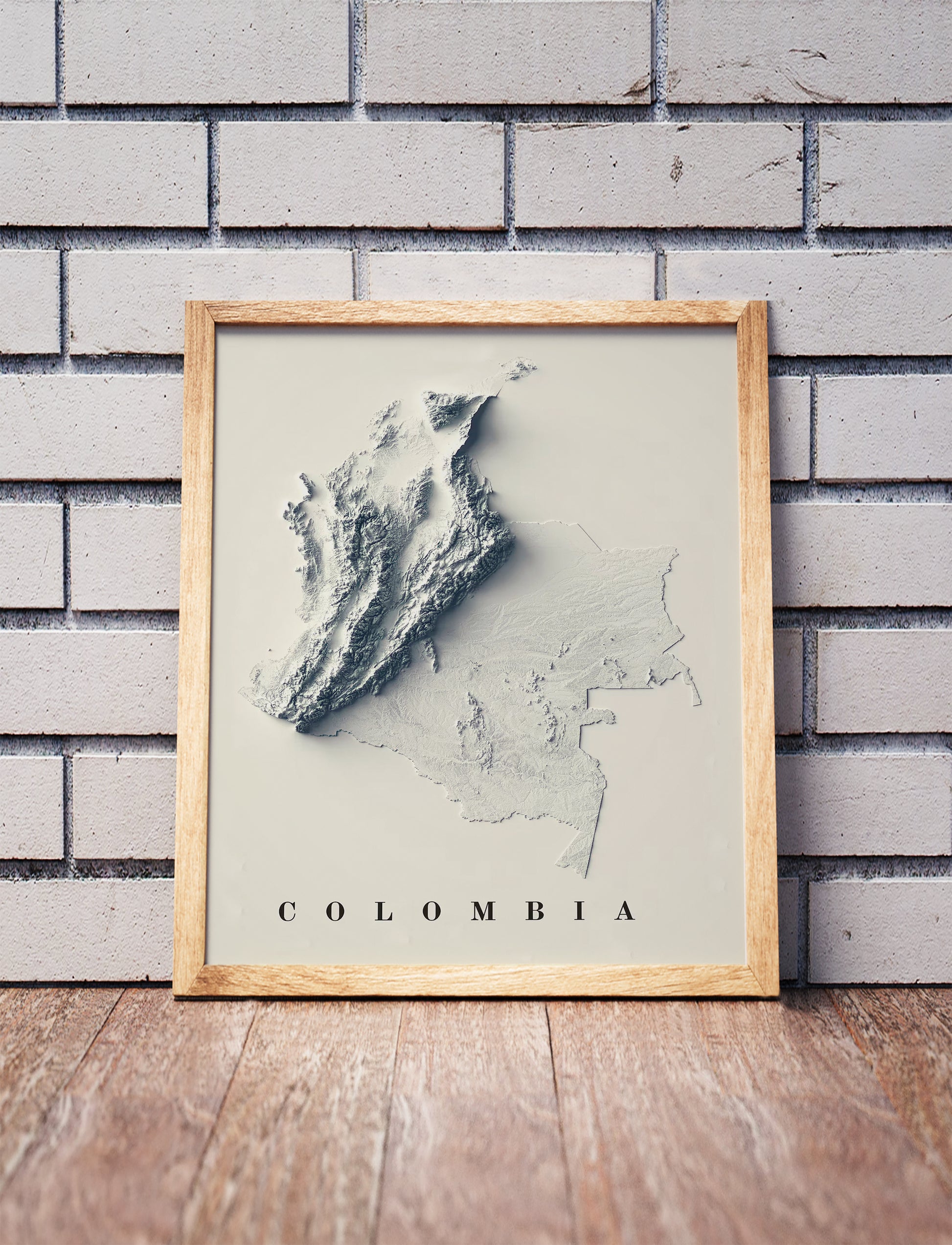 Colombia shaded relief map in a wooden frame. Realistic terrain art print for home decor, displayed against a brick wall