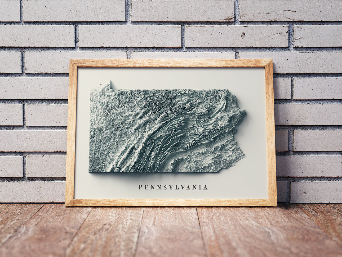 Pennsylvania shaded relief map in a wooden frame. Realistic terrain art print for home decor, displayed against a brick wall