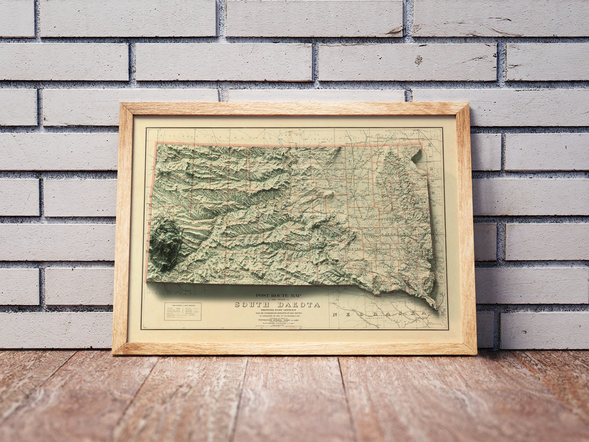 Vintage South Dakota shaded relief map in a wooden frame. Realistic terrain art print for home decor, displayed against a brick wall