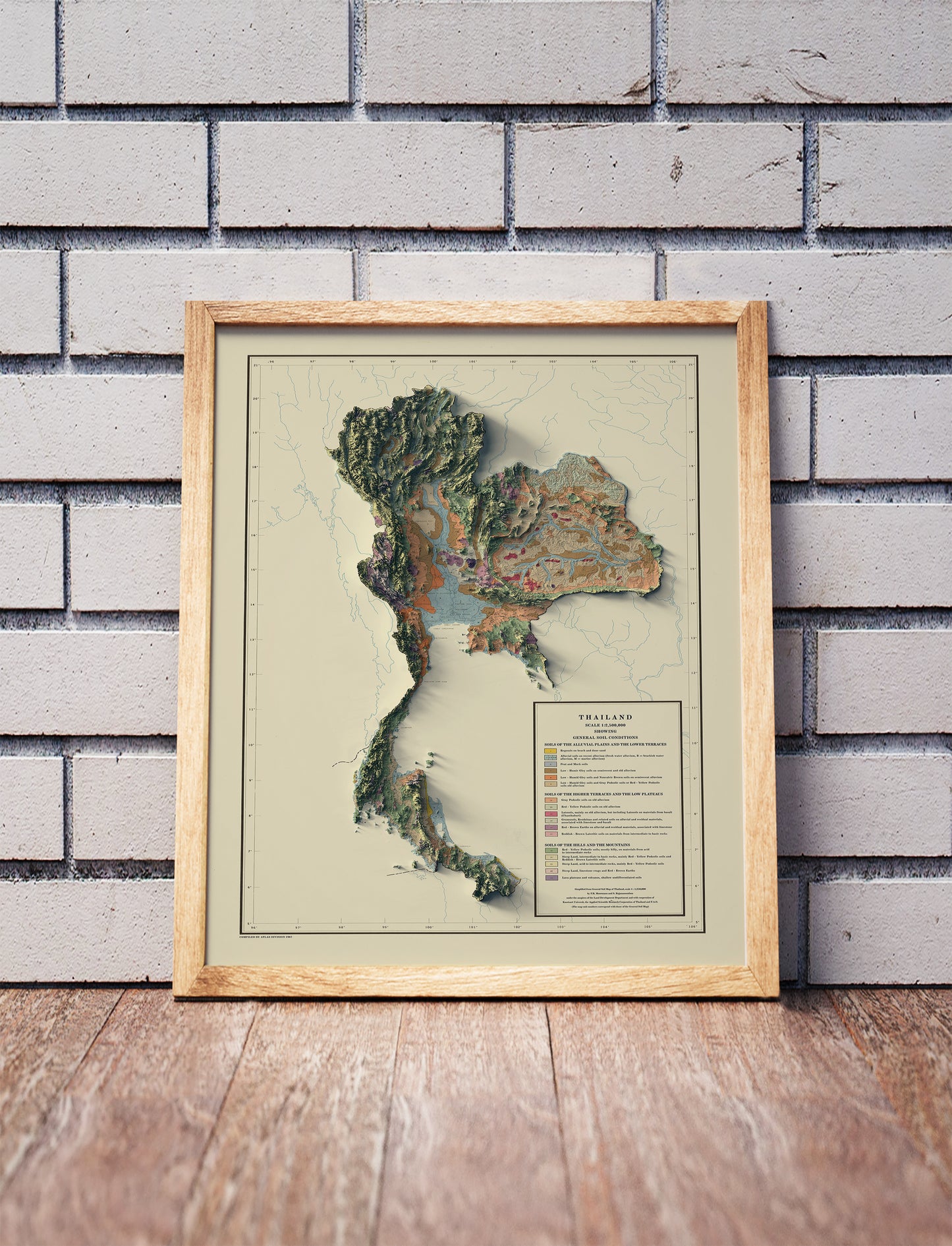 Vintage Thailand shaded relief map in a wooden frame. Realistic terrain art print for home decor, displayed against a brick wall