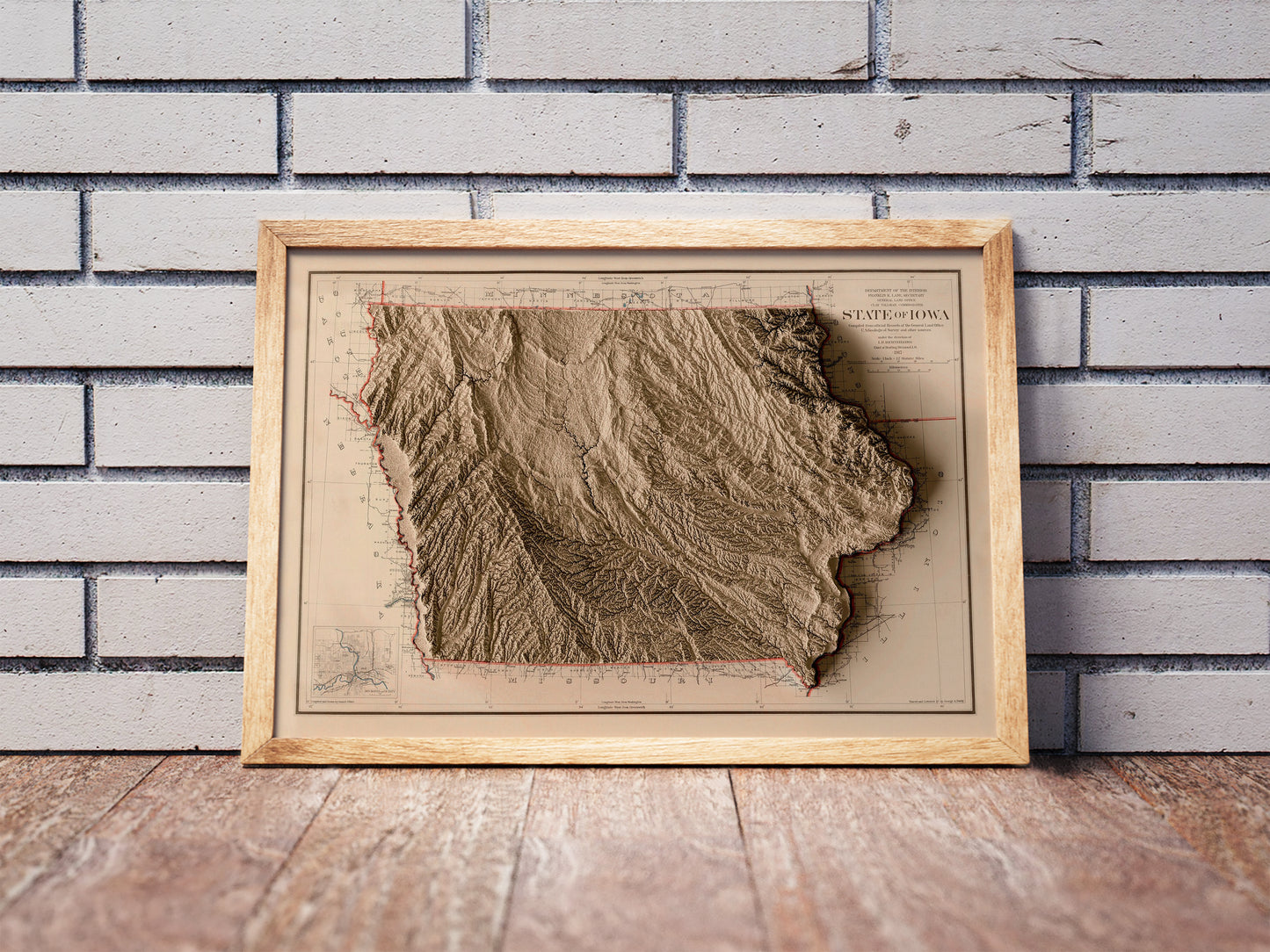 Vintage Iowa shaded relief map in a wooden frame. Realistic terrain art print for home decor, displayed against a brick wall