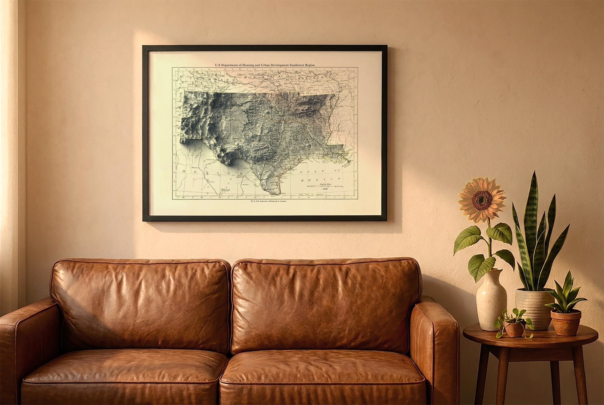 South Central USA vintage relief map in a black frame above a brown leather sofa. Boho living room with warm sunlight, sunflower, and indoor plants on a wooden side table