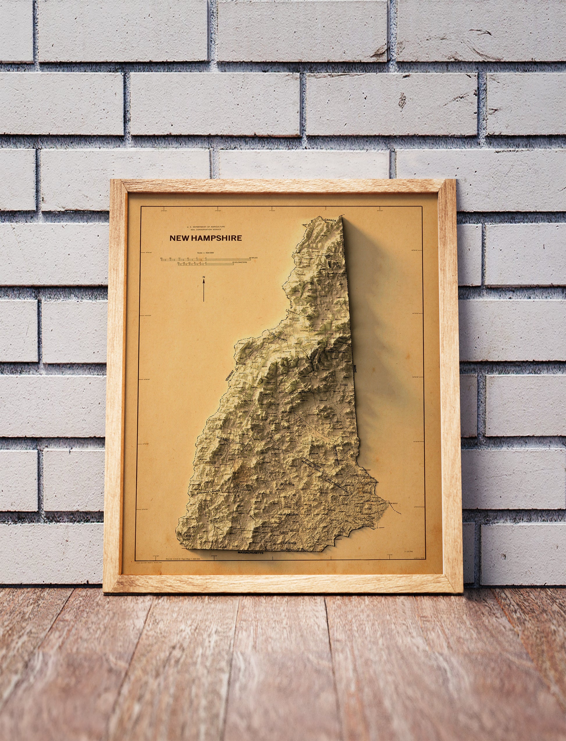 Vintage New Hampshire shaded relief map in a wooden frame. Realistic terrain art print for home decor, displayed against a brick wall