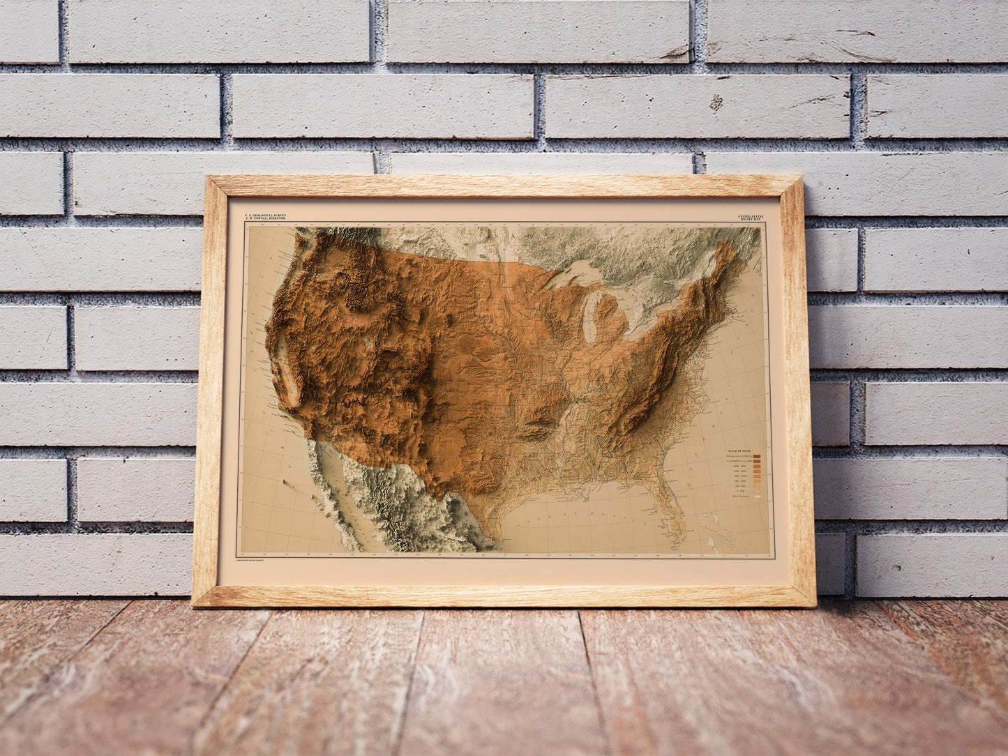 Vintage United States shaded relief map in a wooden frame. Realistic terrain art print for home decor, displayed against a brick wall