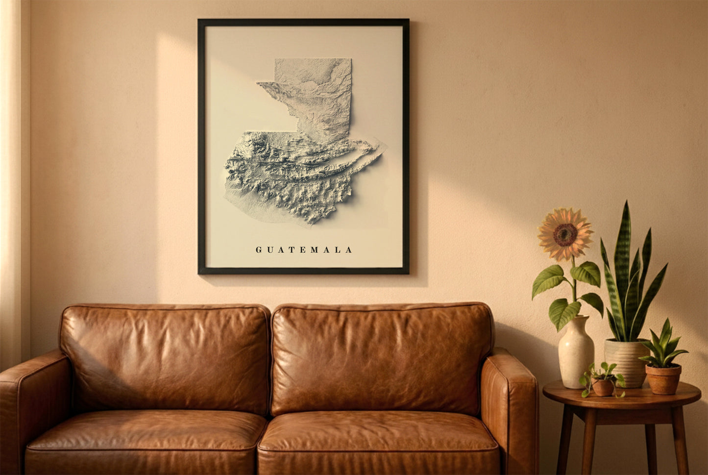 Guatemala relief map in a black frame above a brown leather sofa. Boho living room with warm sunlight, sunflower, and indoor plants on a wooden side table