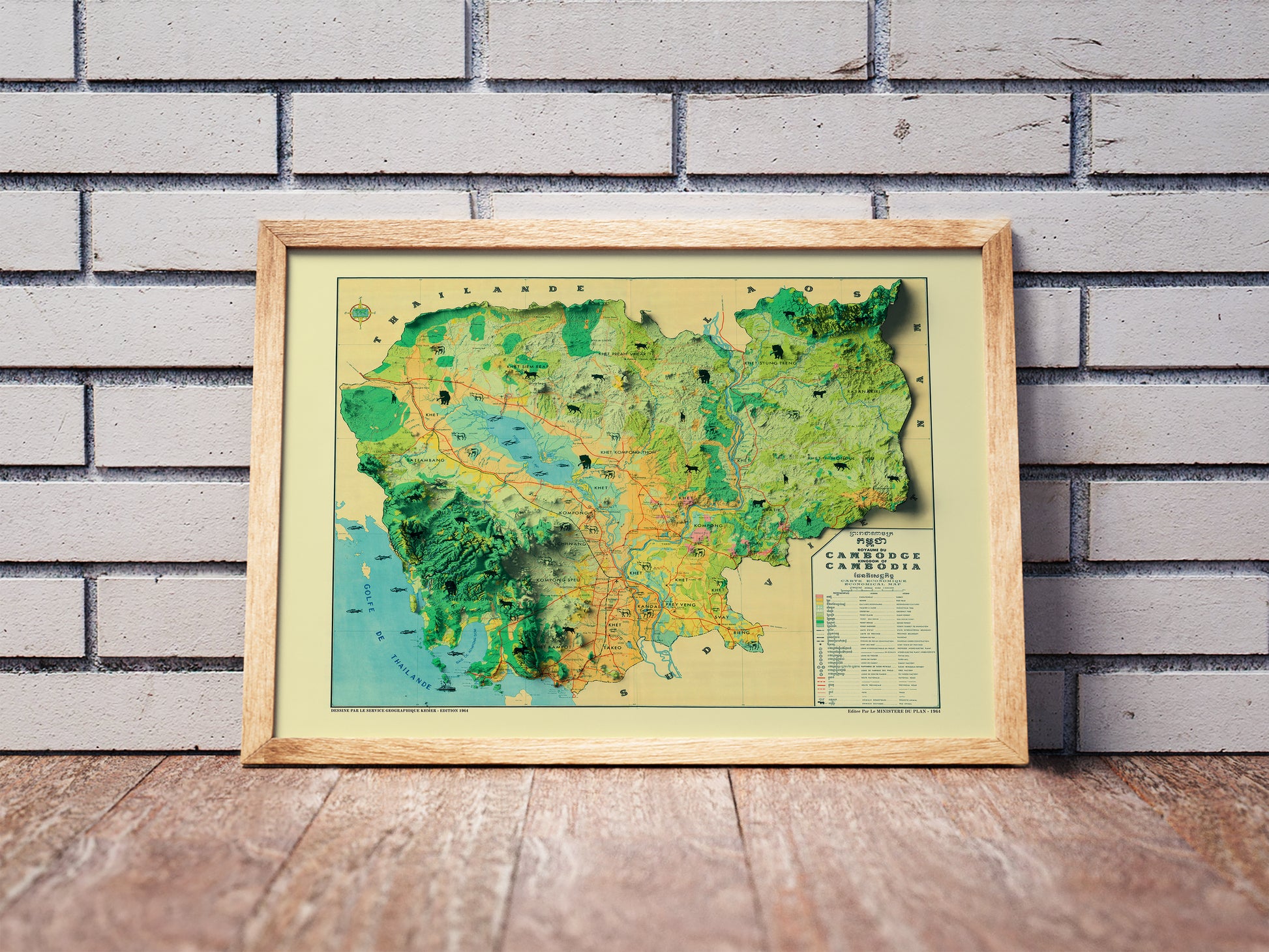 Vintage Cambodia shaded relief map in a wooden frame. Realistic terrain art print for home decor, displayed against a brick wall