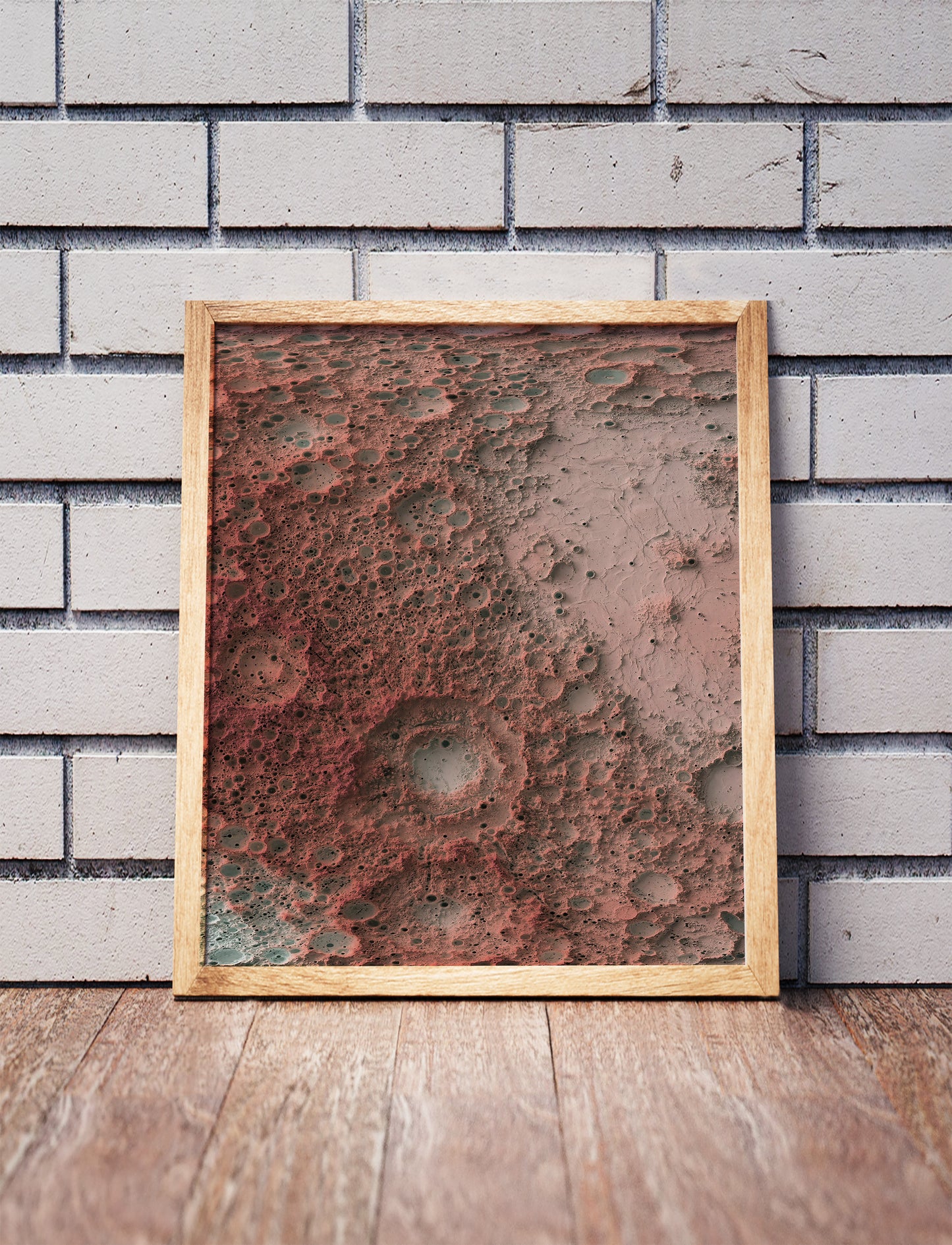 Moon shaded relief map in a wooden frame. Realistic terrain art print for home decor, displayed against a brick wall