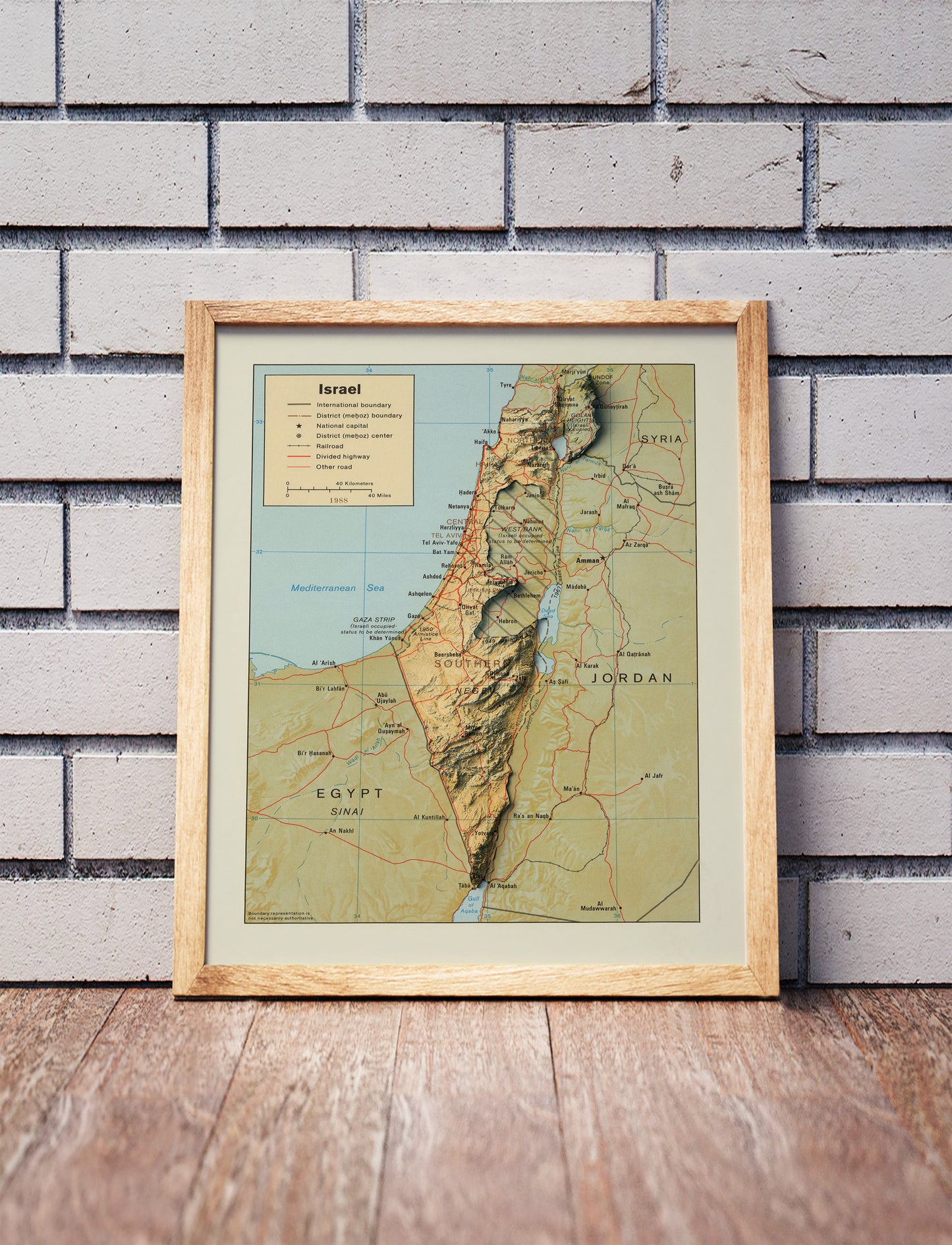Vintage Israel shaded relief map in a wooden frame. Realistic terrain art print for home decor, displayed against a brick wall
