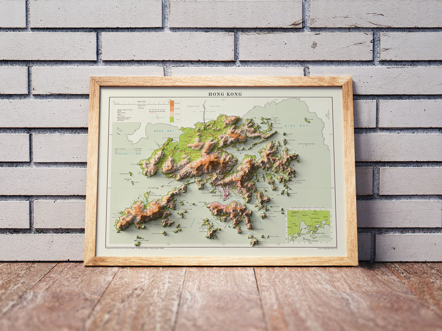 Vintage Hong Kong shaded relief map in a wooden frame. Realistic terrain art print for home decor, displayed against a brick wall